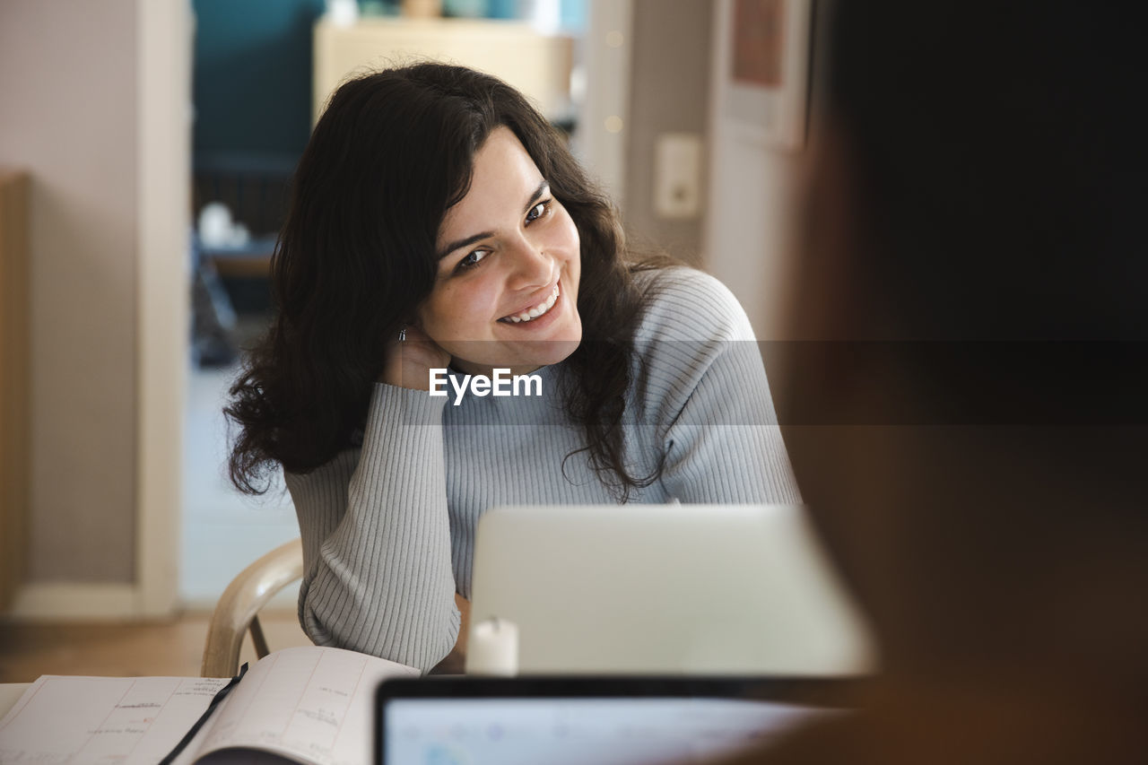 Smiling woman with hand in hair sitting with laptop at home