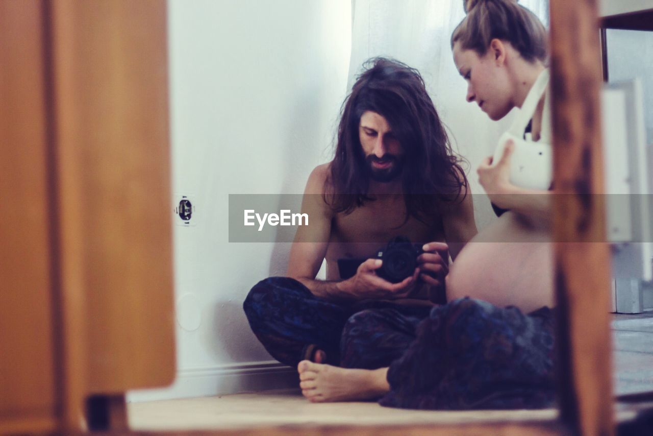 Pregnant woman sitting by shirtless man on floor at home