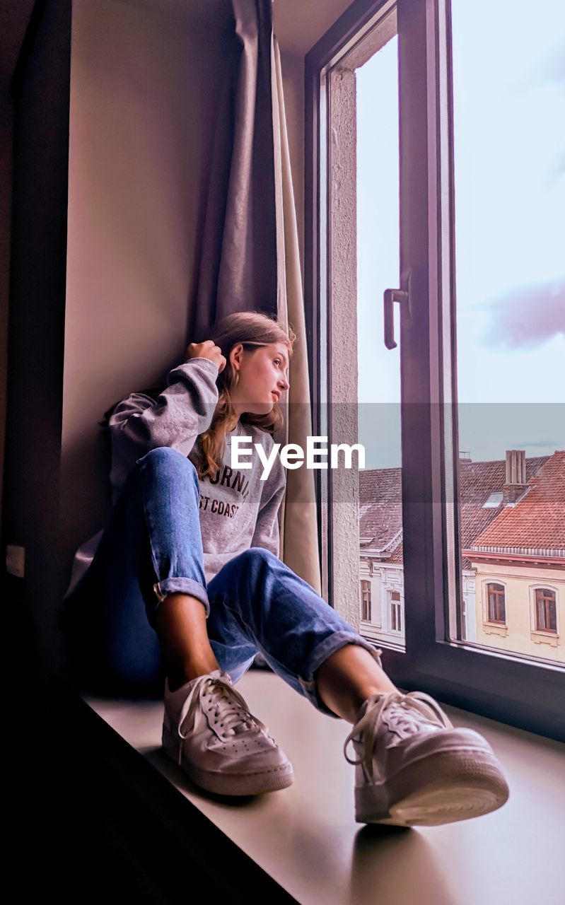 Girl looking through window while sitting at home