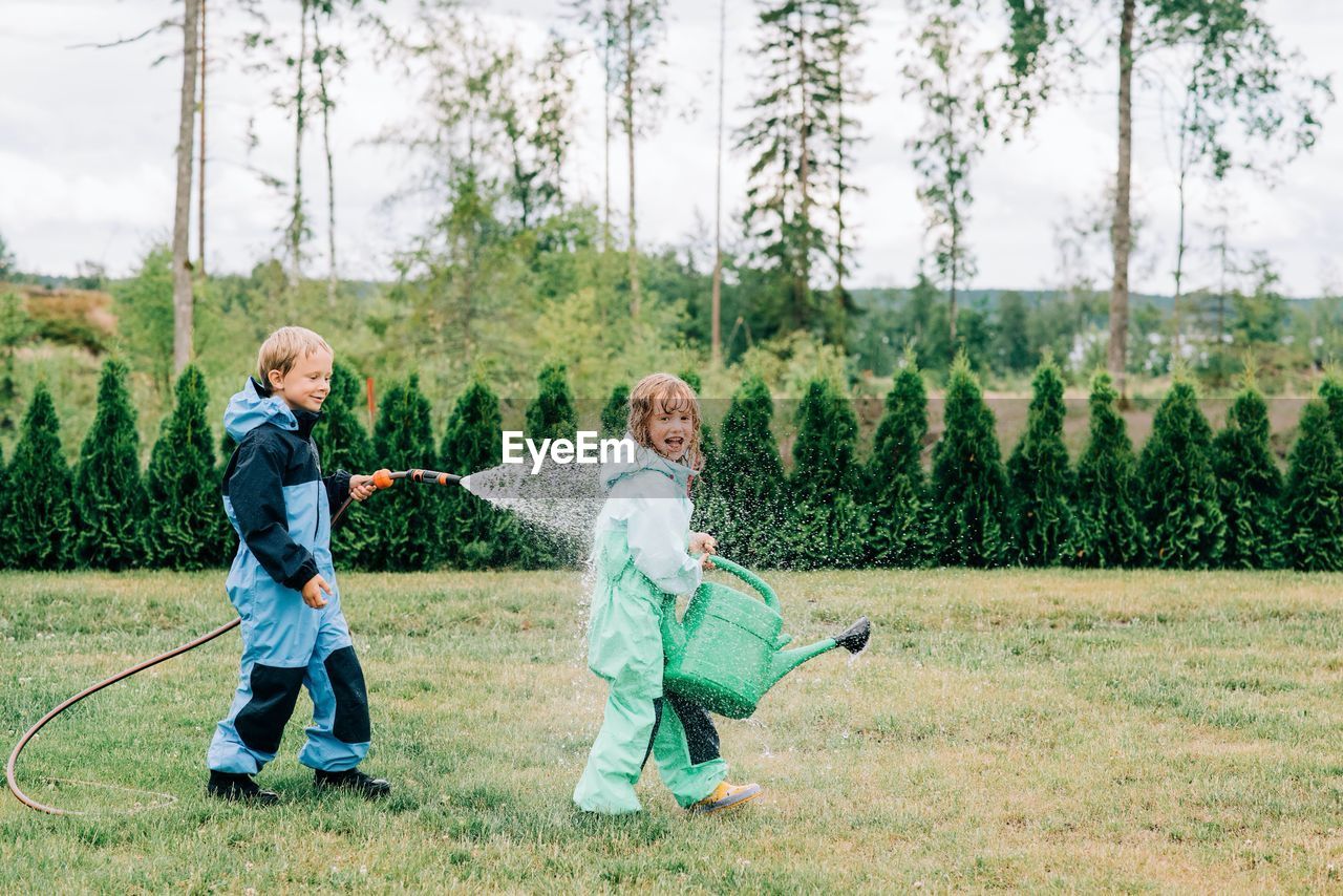 Brother and sister playing in the rain with a hose and watering can