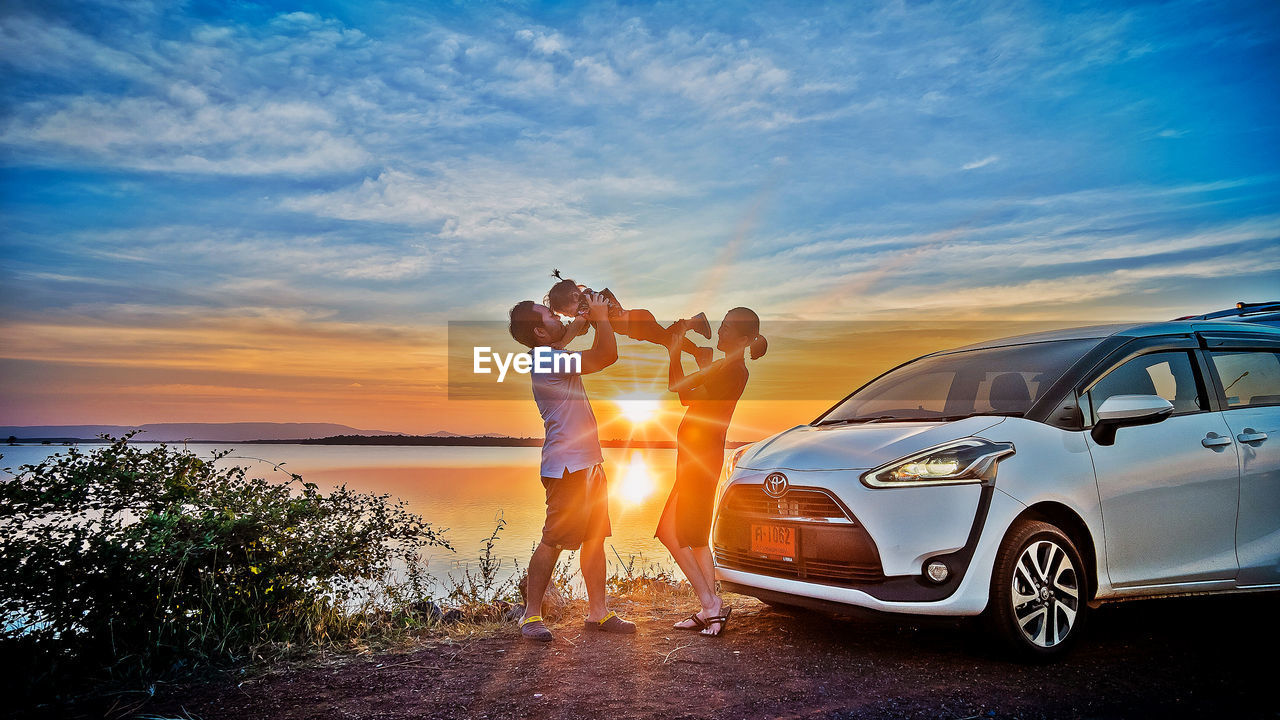 PEOPLE STANDING BY CAR AGAINST SKY