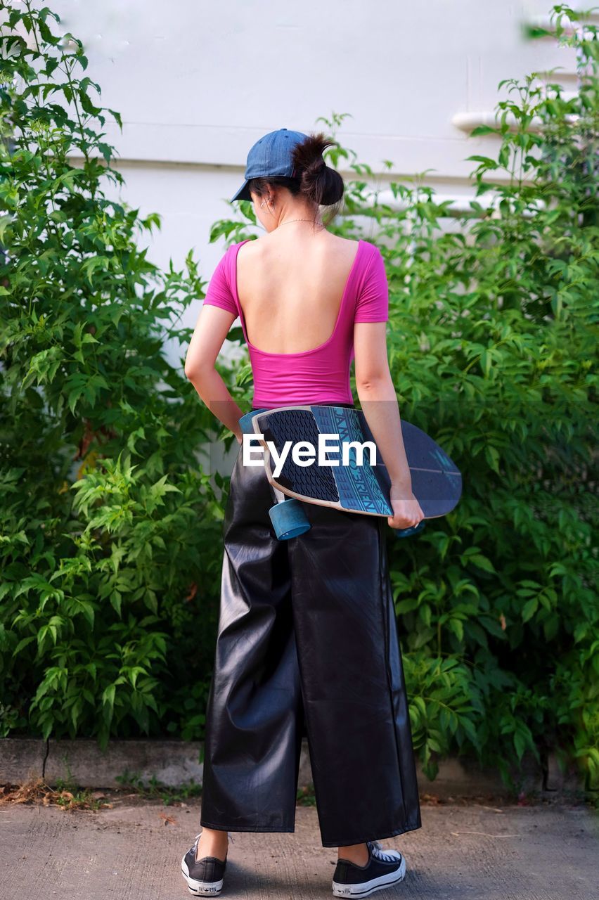 FULL LENGTH OF YOUNG WOMAN STANDING AGAINST PLANTS