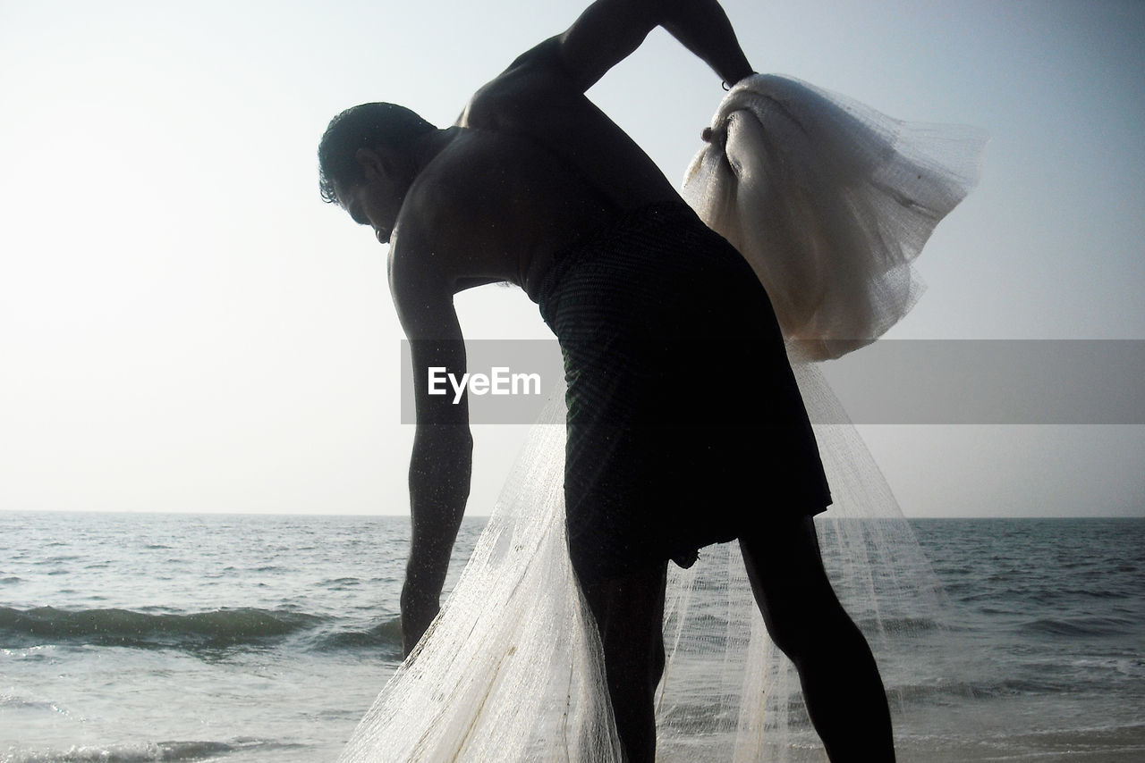 Fisherman holding net while standing at beach against sky