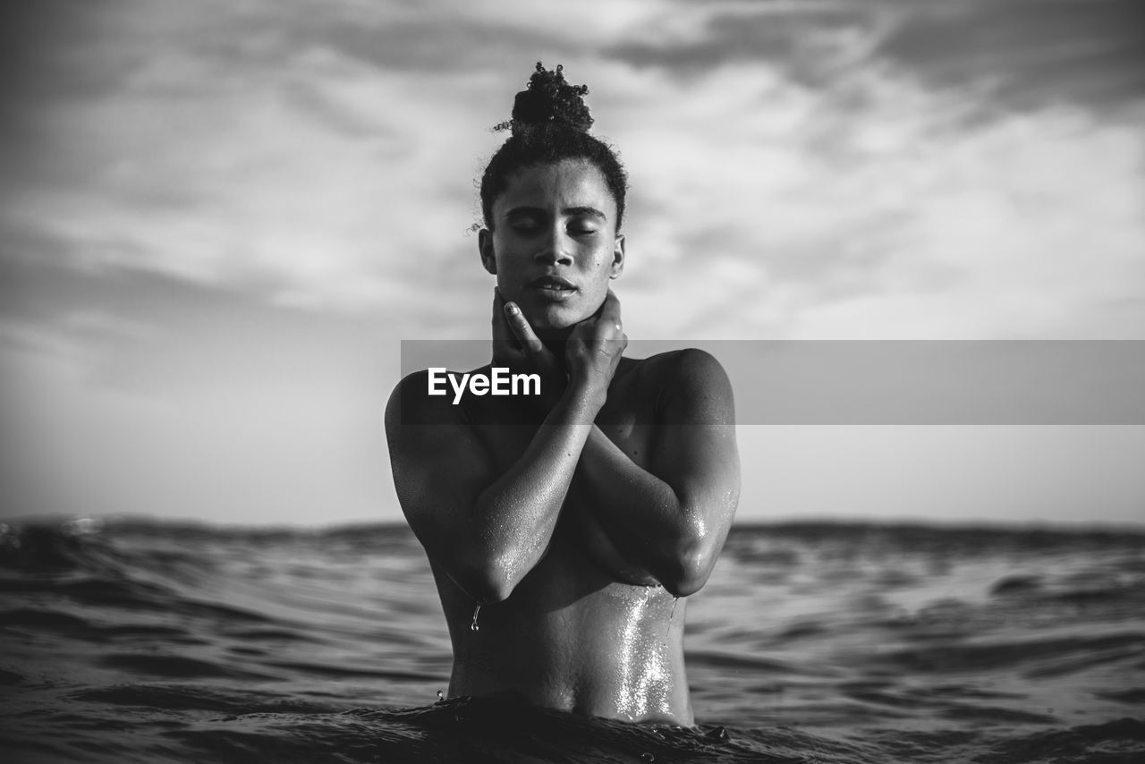 Shirtless woman in sea against sky during sunset