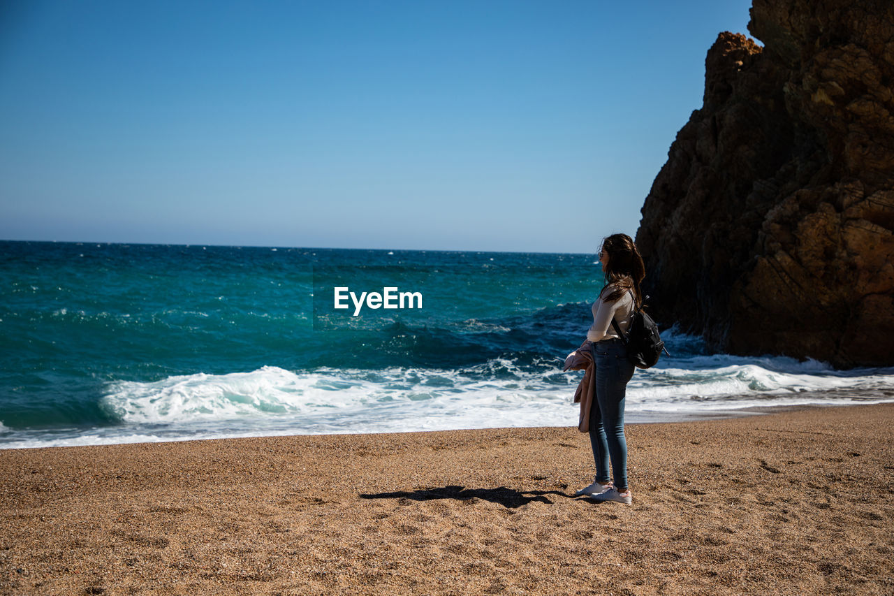 WOMAN STANDING ON BEACH AGAINST SEA