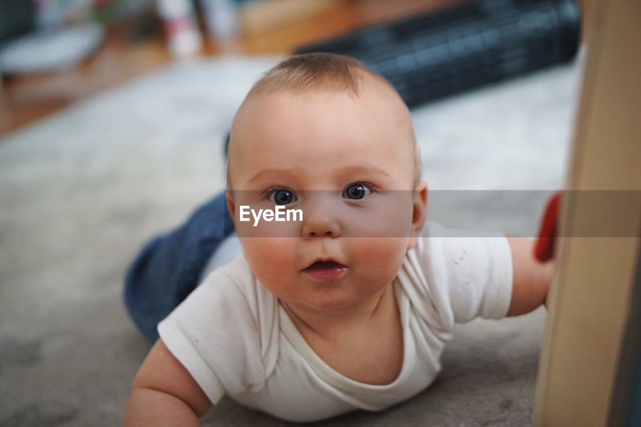 Portrait of cute baby girl lying on carpet at home