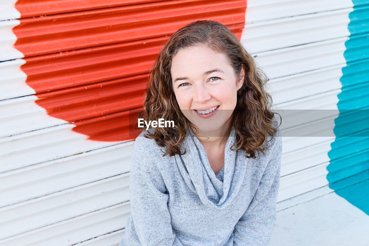 Portrait of smiling woman sitting against shutter