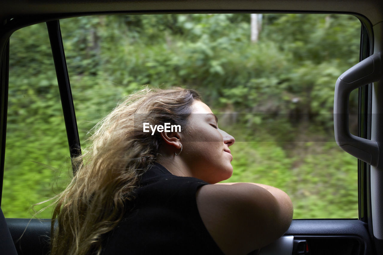 Young woman leaning out car window from car interior