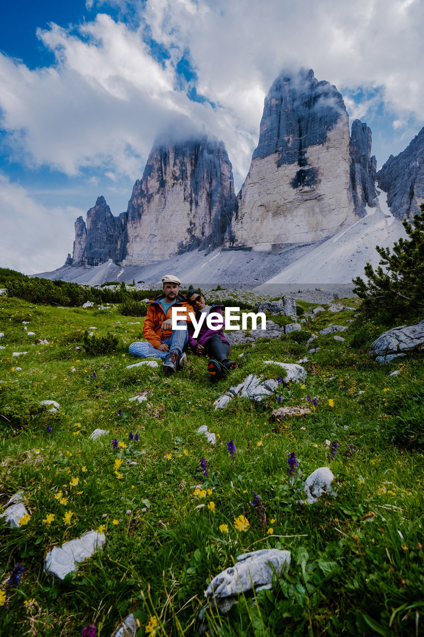 PEOPLE SITTING BY PLANTS AGAINST MOUNTAINS