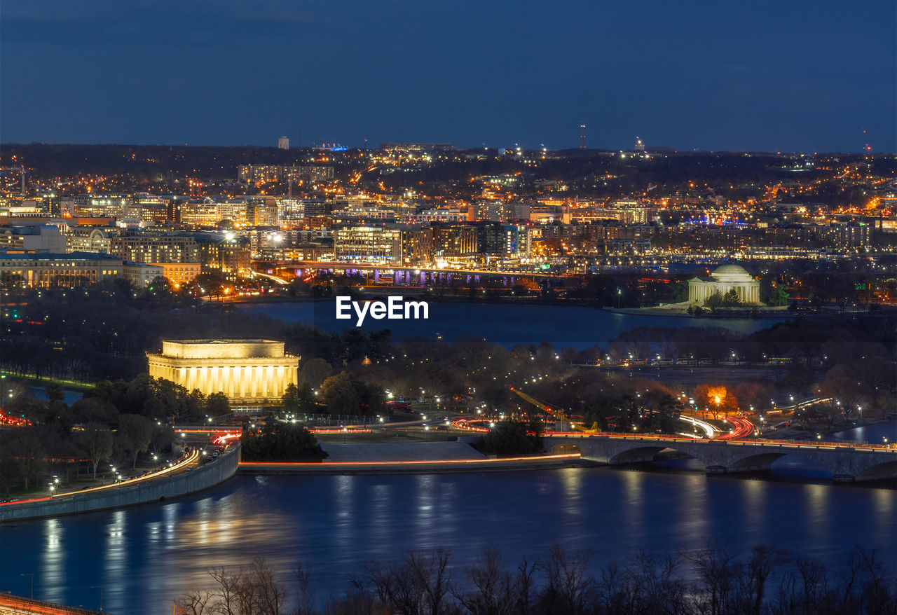 Illuminated buildings by river against sky at night