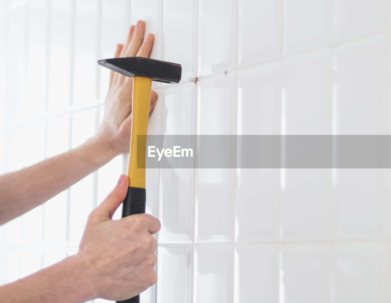 The hands of a young caucasian guy hammer a dowel into a drilled hole on a tiled wall