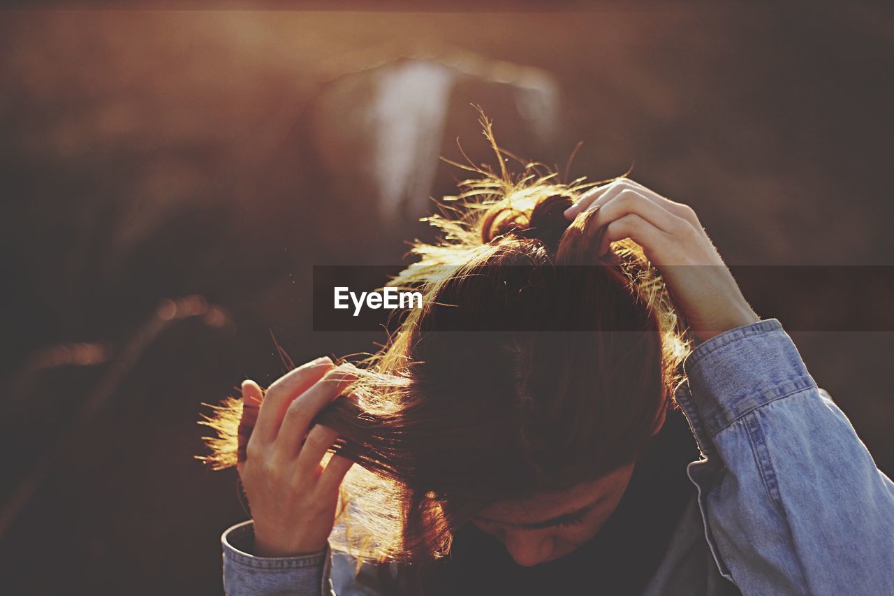 Close-up of young woman tying hair while standing outdoors during sunset