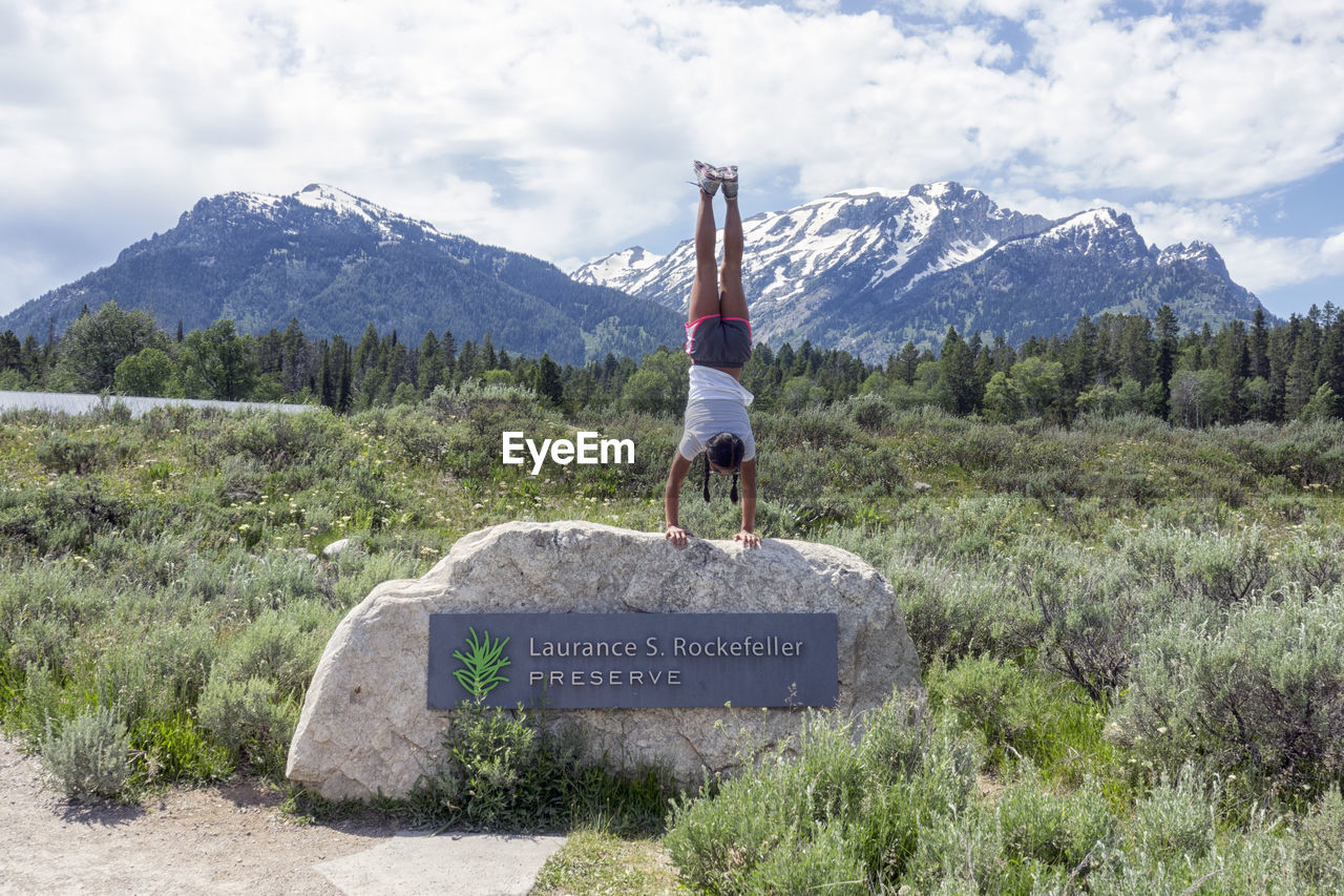 REAR VIEW OF MAN STANDING ON MOUNTAIN ROAD AGAINST SKY