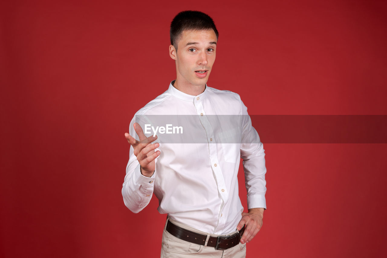 one person, studio shot, portrait, colored background, adult, men, red, young adult, indoors, looking at camera, waist up, standing, clothing, front view, formal wear, red background, button down shirt, person, emotion, three quarter length, copy space