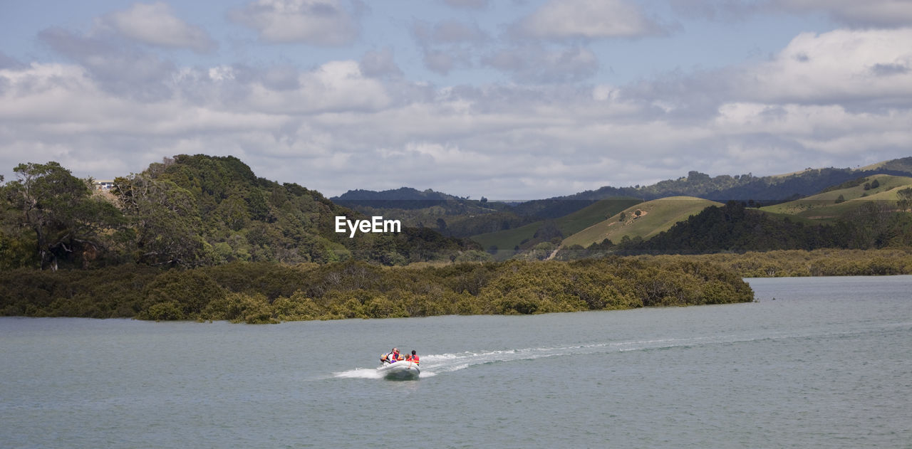 People riding boat on river by mountain against sky