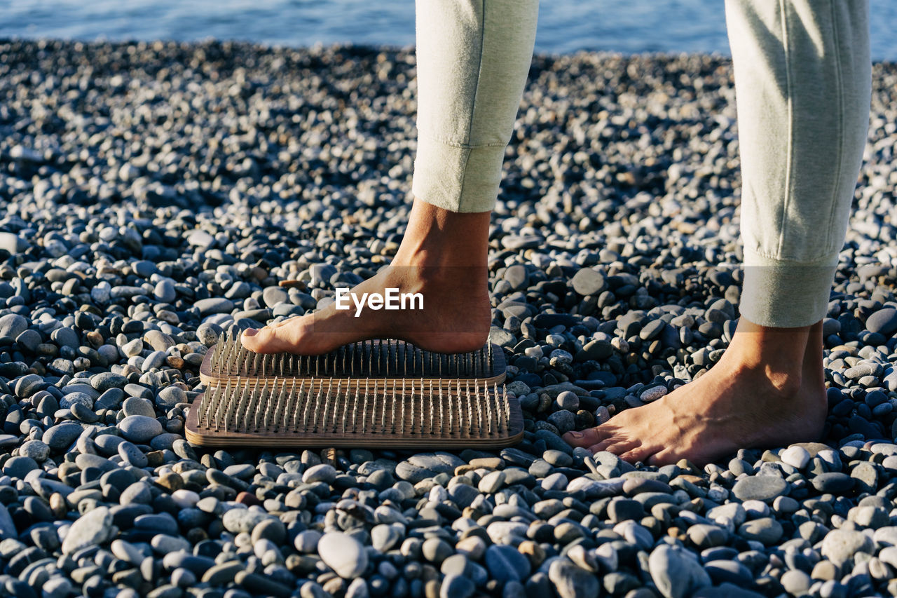 Barefoot female foot stands on a wooden board with nails for concentration practice by seashore