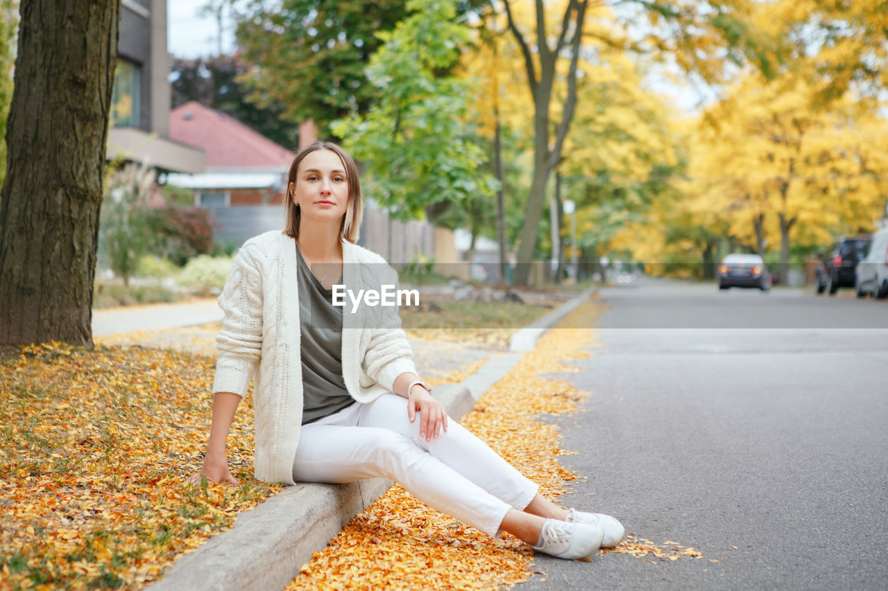 Beautiful middle age caucasian woman with short hair sitting in autumn fall street outdoor. 