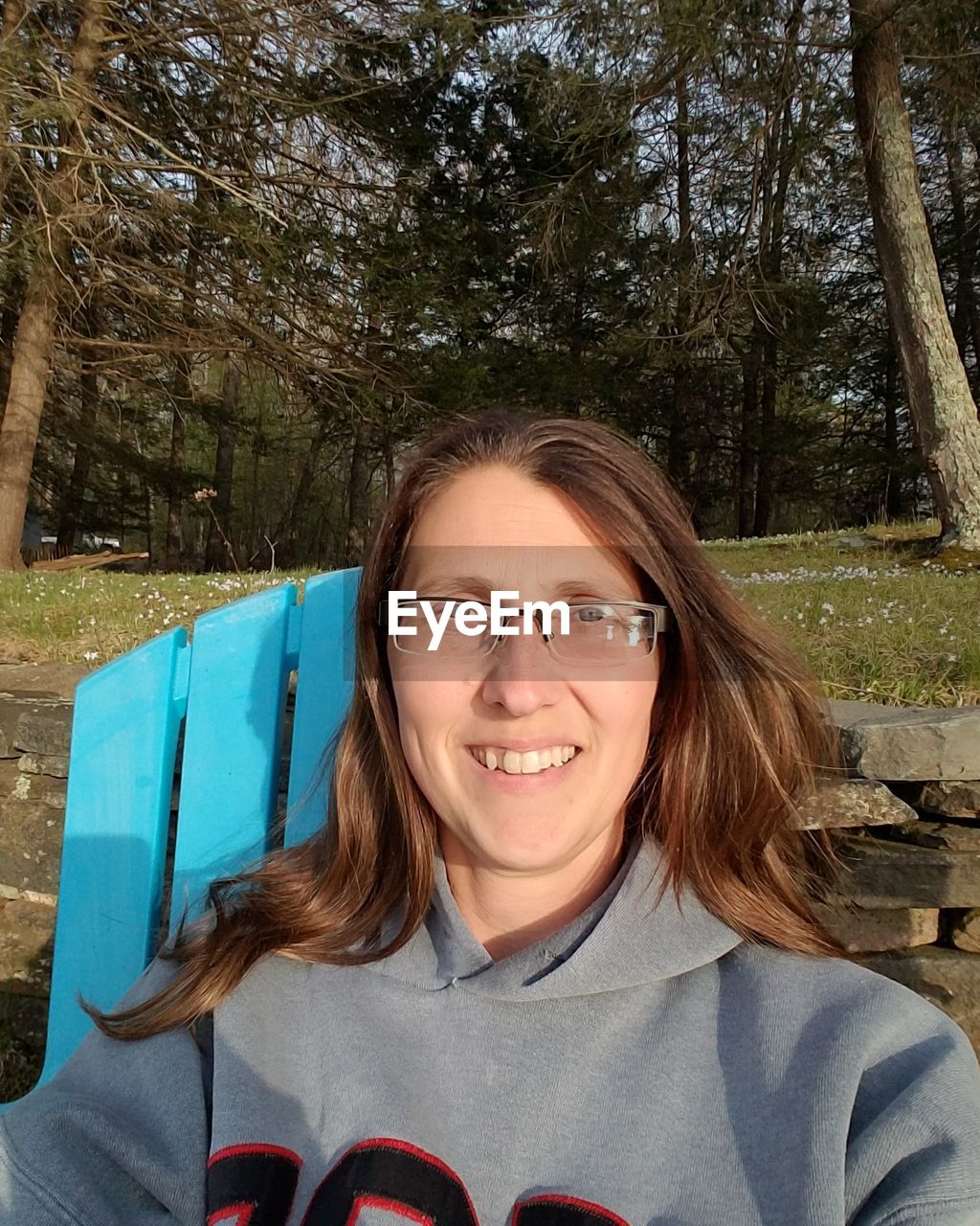 Portrait of smiling woman sitting on chair against trees