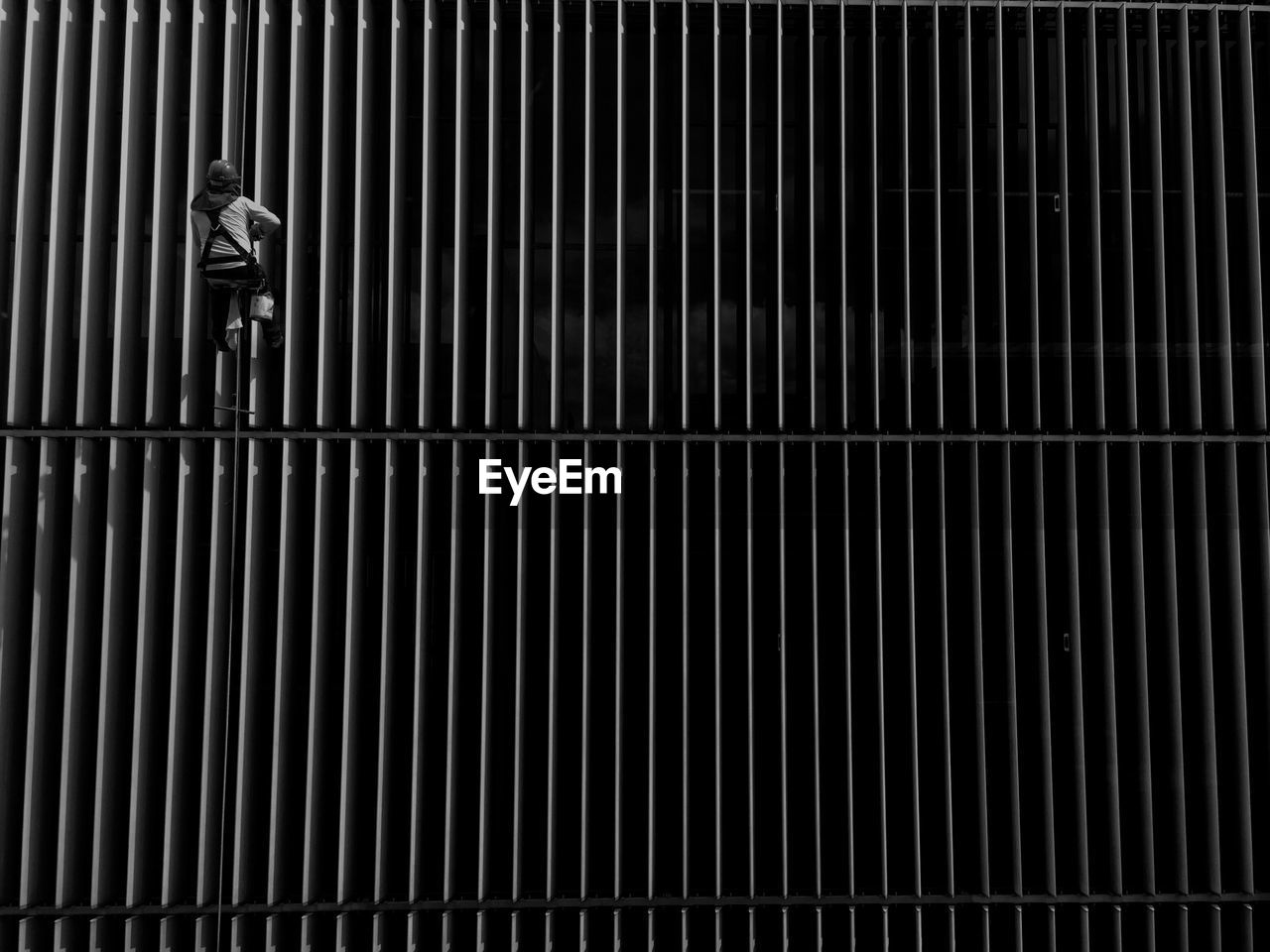 Rear view of window washer hanging from rope against building