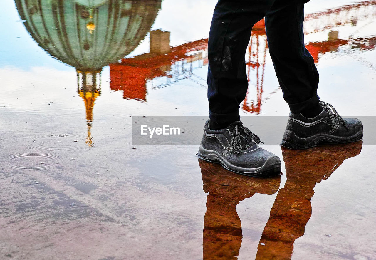 Low section of man walking by berlin cathedral reflection on walkway in rainy season