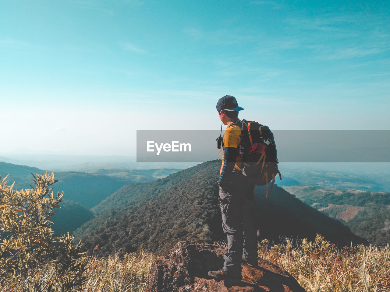 MAN STANDING ON MOUNTAIN LOOKING AT VIEW