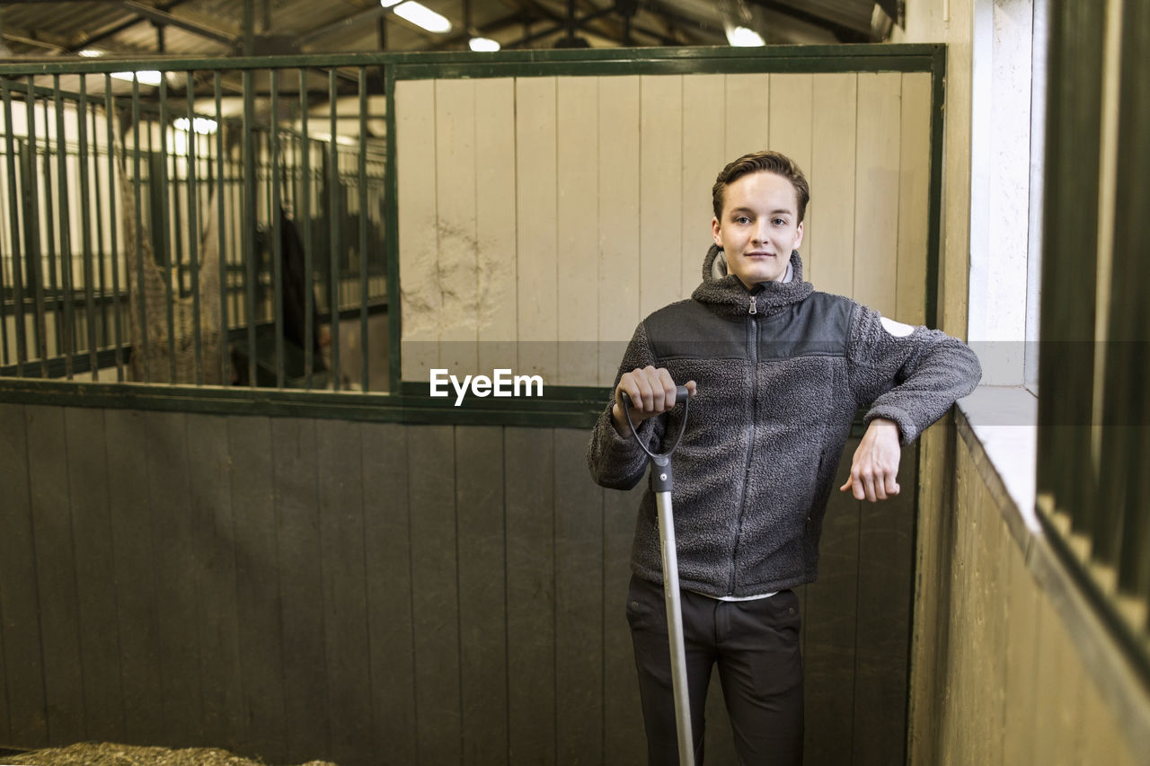 Portrait of confident young man with pitchfork in horse stable