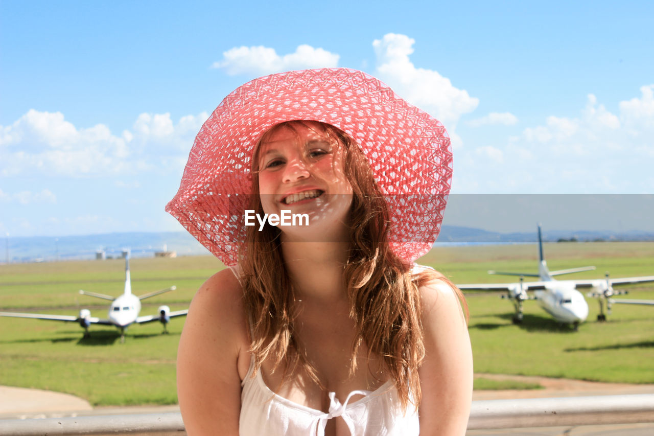 Portrait of smiling beautiful woman standing by airplanes on field against sky