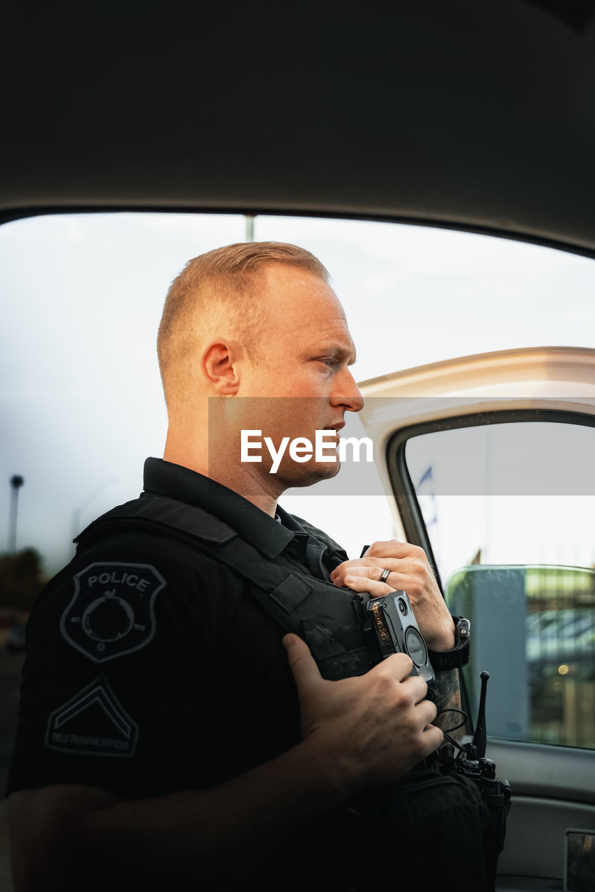 White male police officer standing outside of vehicle to investigate a situation