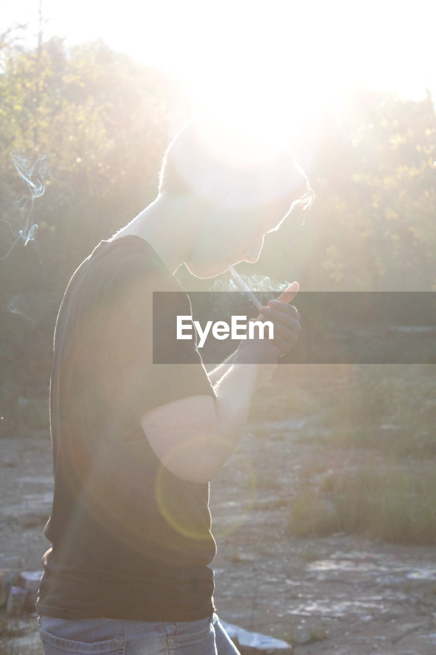 Side view of young man smoking cigarette on sunny day