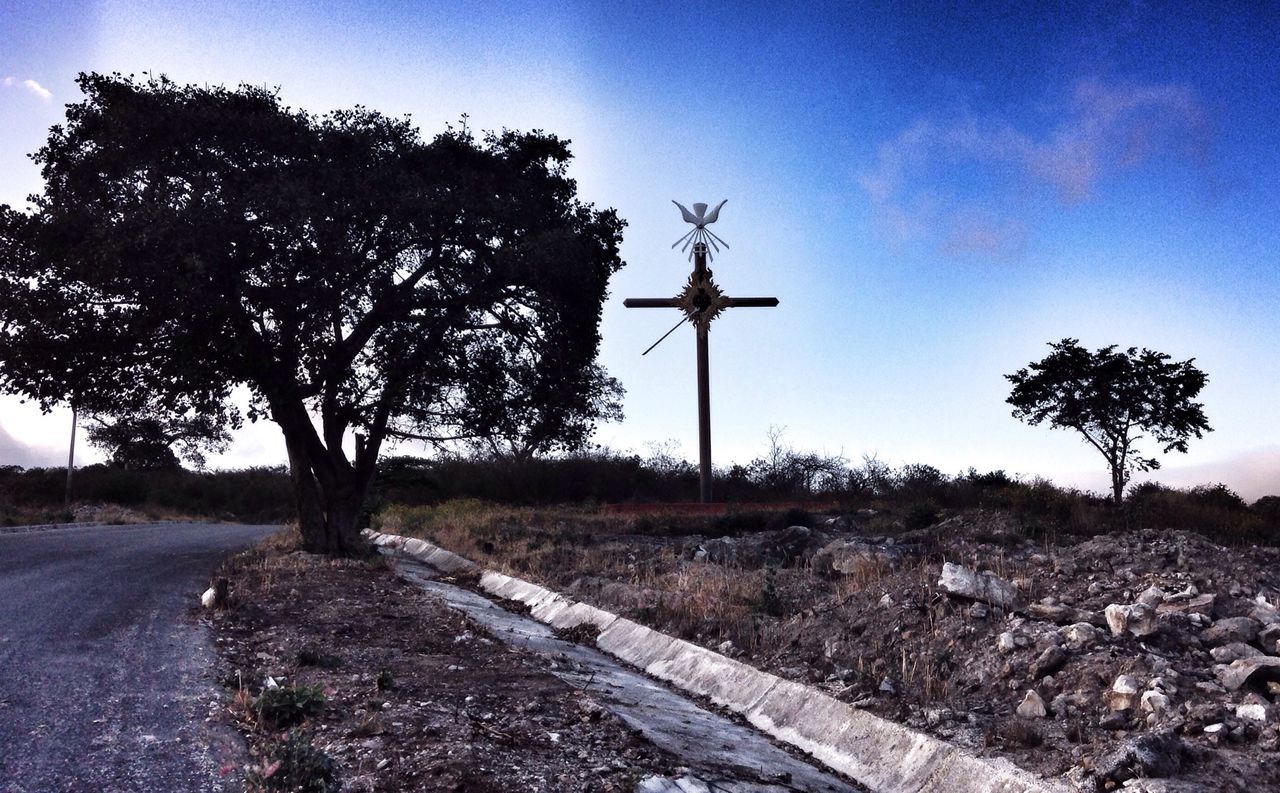 Cross on field by road against sky