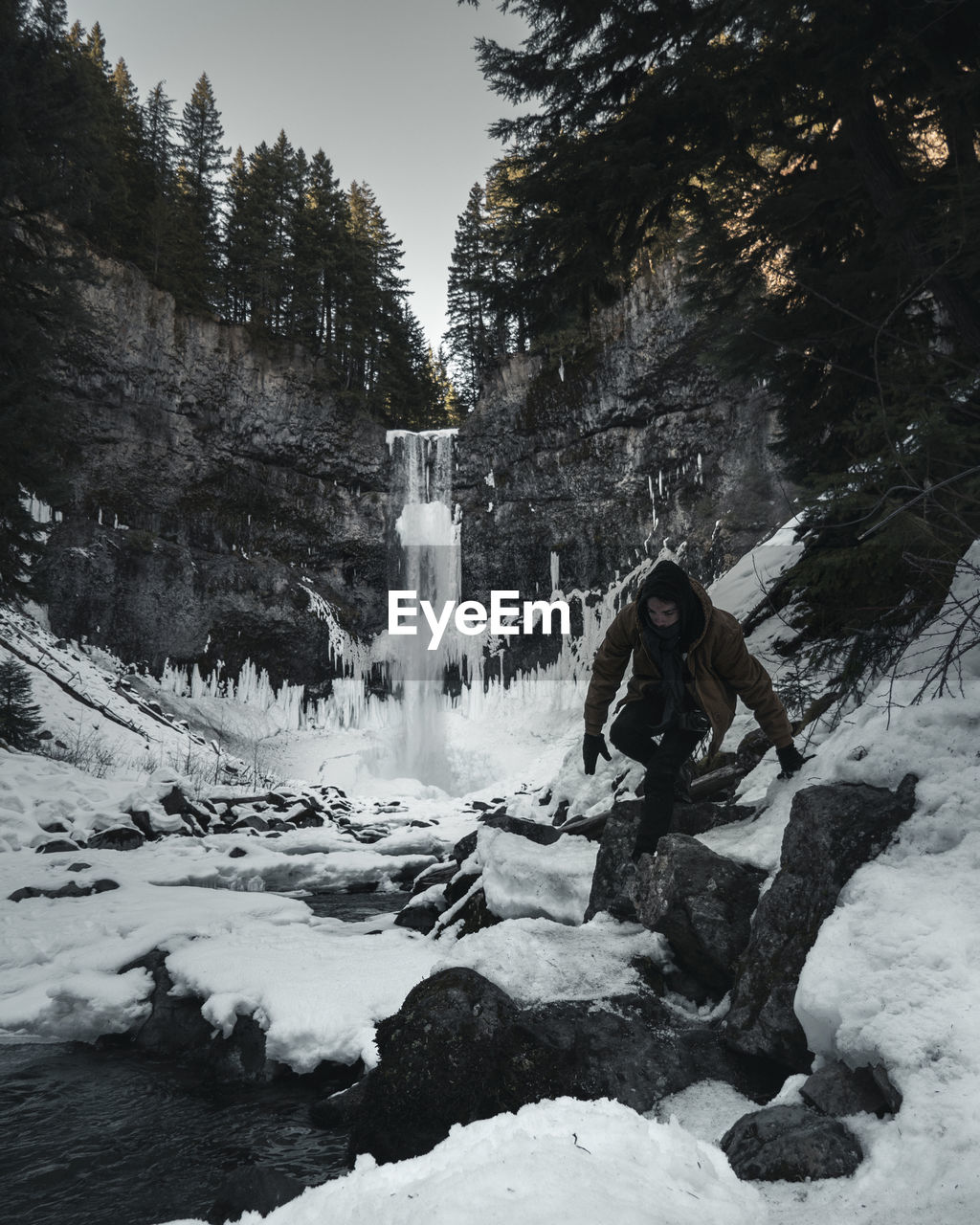 Man walking on snow covered land against waterfall