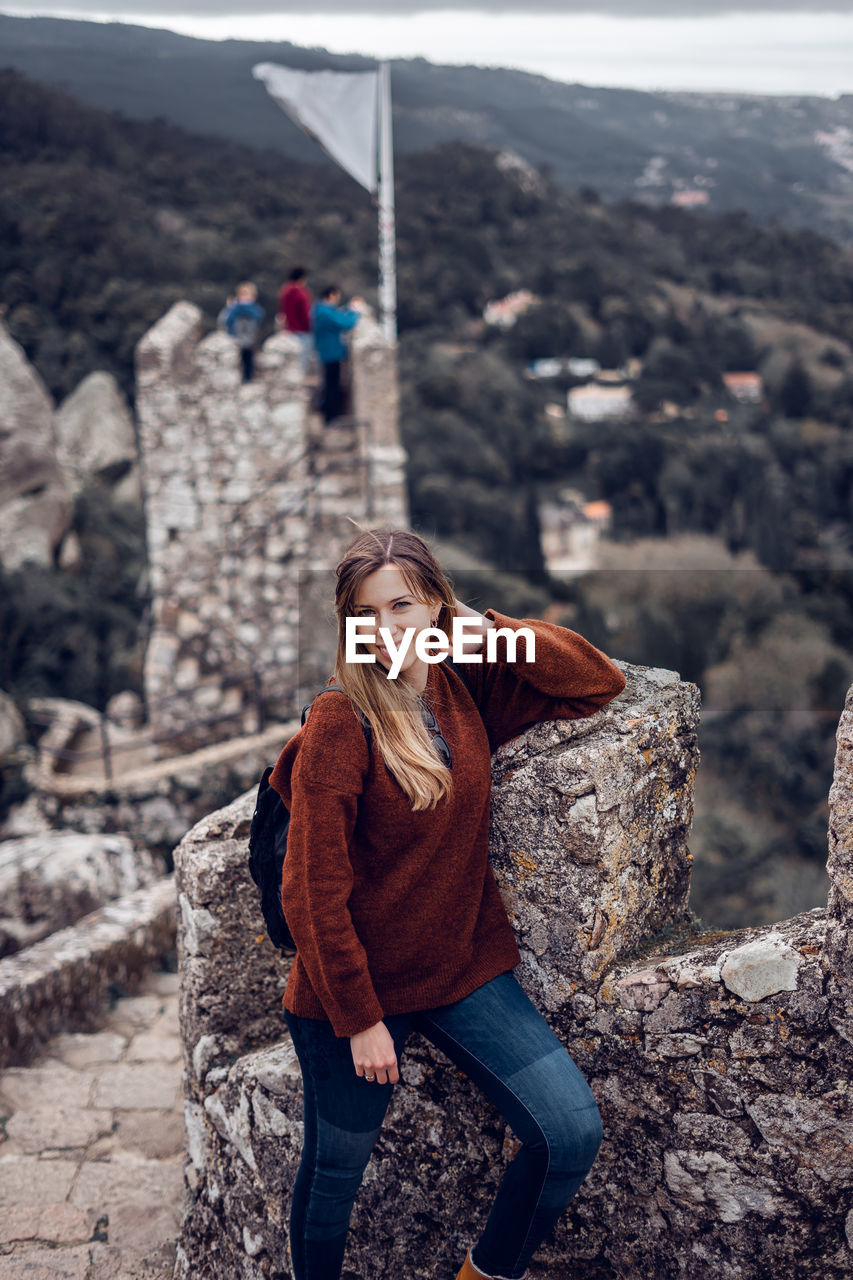 Portrait of young woman standing on stairs in tower against sky