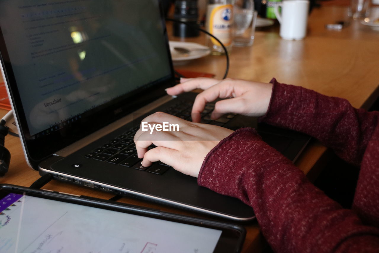 MIDSECTION OF WOMAN USING MOBILE PHONE IN LAPTOP