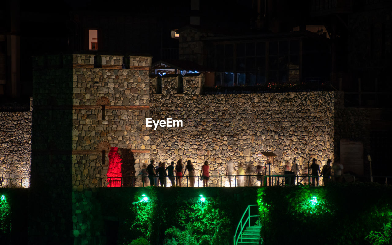 ILLUMINATED LIGHTS HANGING ON WALL IN CITY