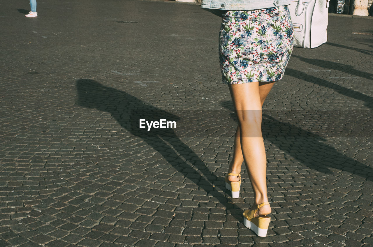 Low section of fashionable woman wearing sandals while walking on cobblestone