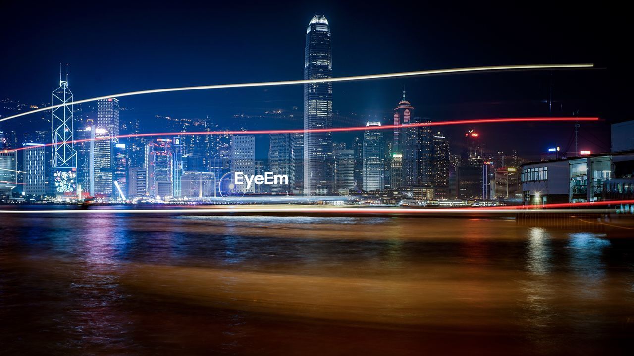 Light trails over victoria harbour against illuminated city at night