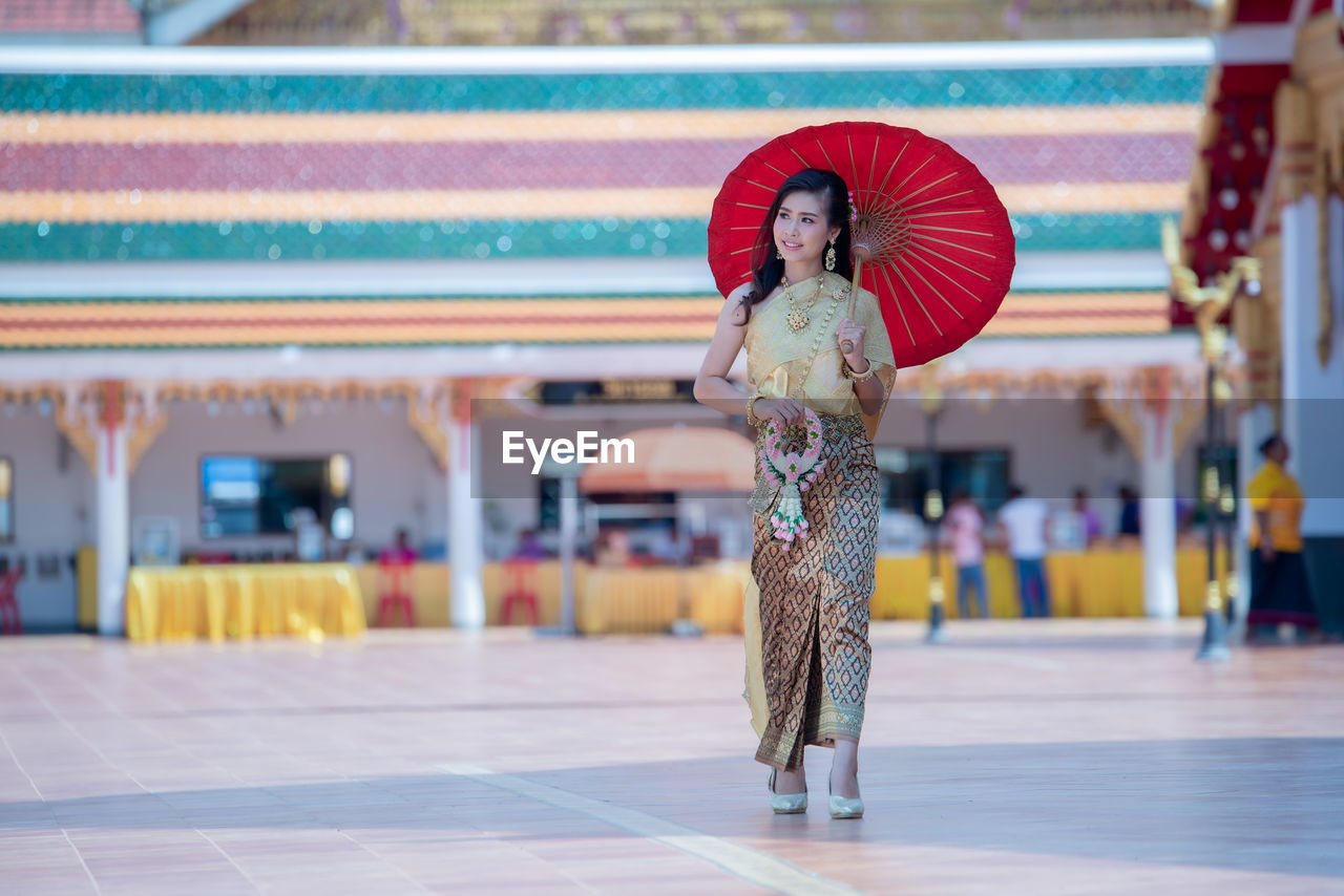 Woman wearing traditional clothing holding umbrella while walking on footpath