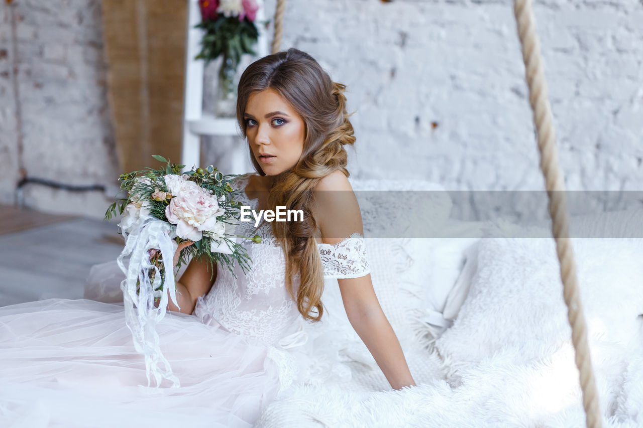 YOUNG WOMAN HOLDING FLOWER BOUQUET AGAINST WALL