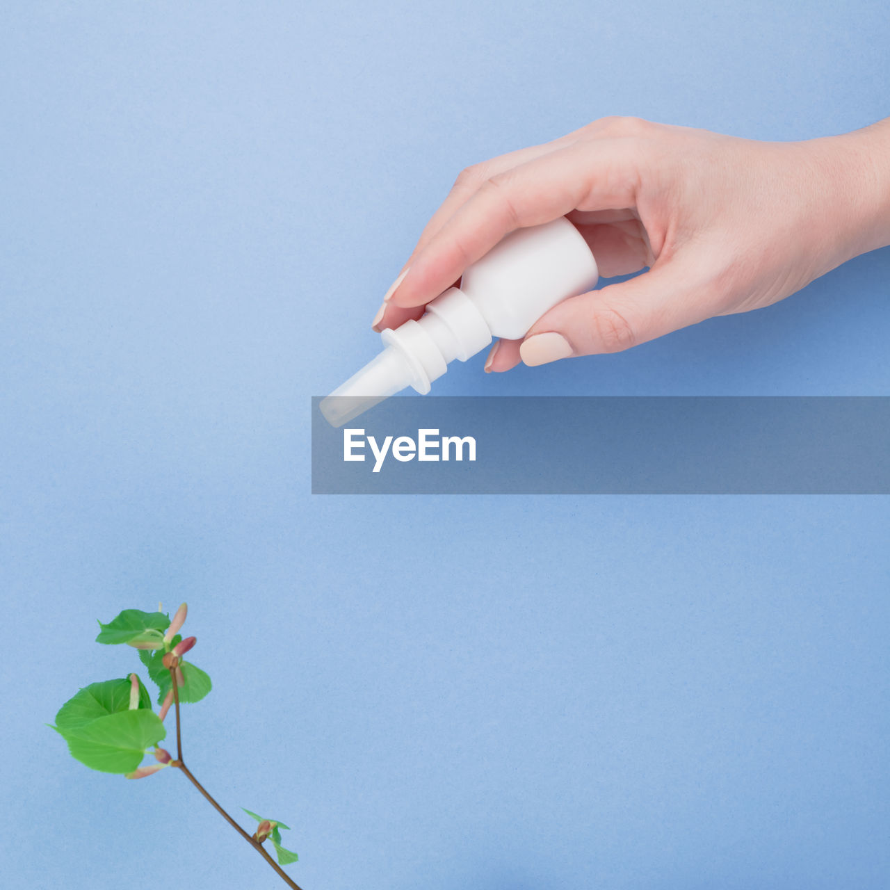 Close-up of hand holding eyedropper over plant against blue background