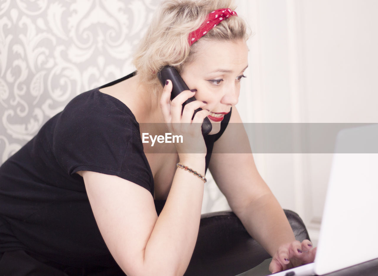 Female hairdresser talking on cordless phone while using laptop in salon