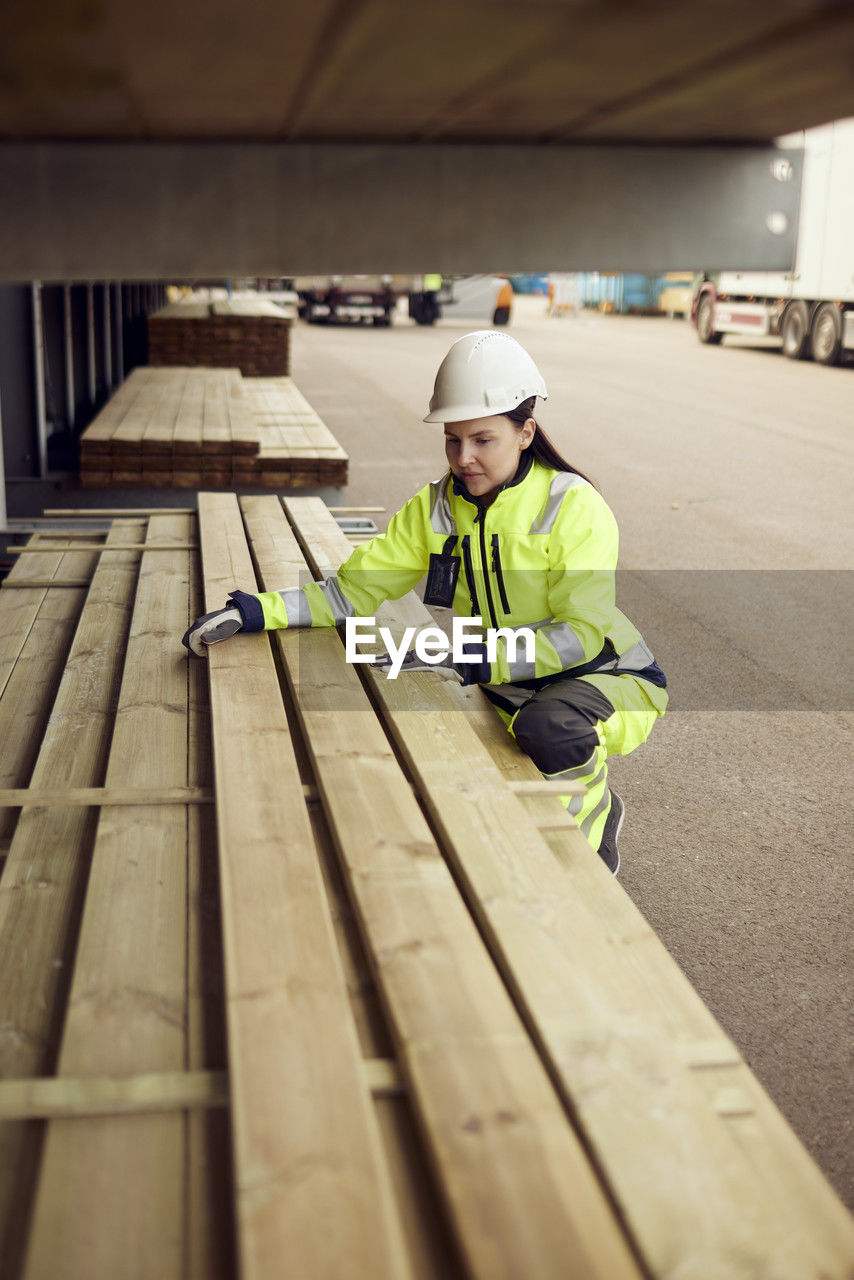 Female worker in protective workwear arranging planks at lumber industry