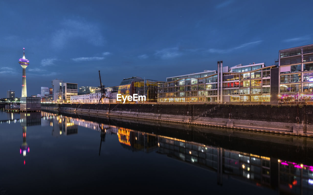 Reflection of illuminated buildings in river against sky