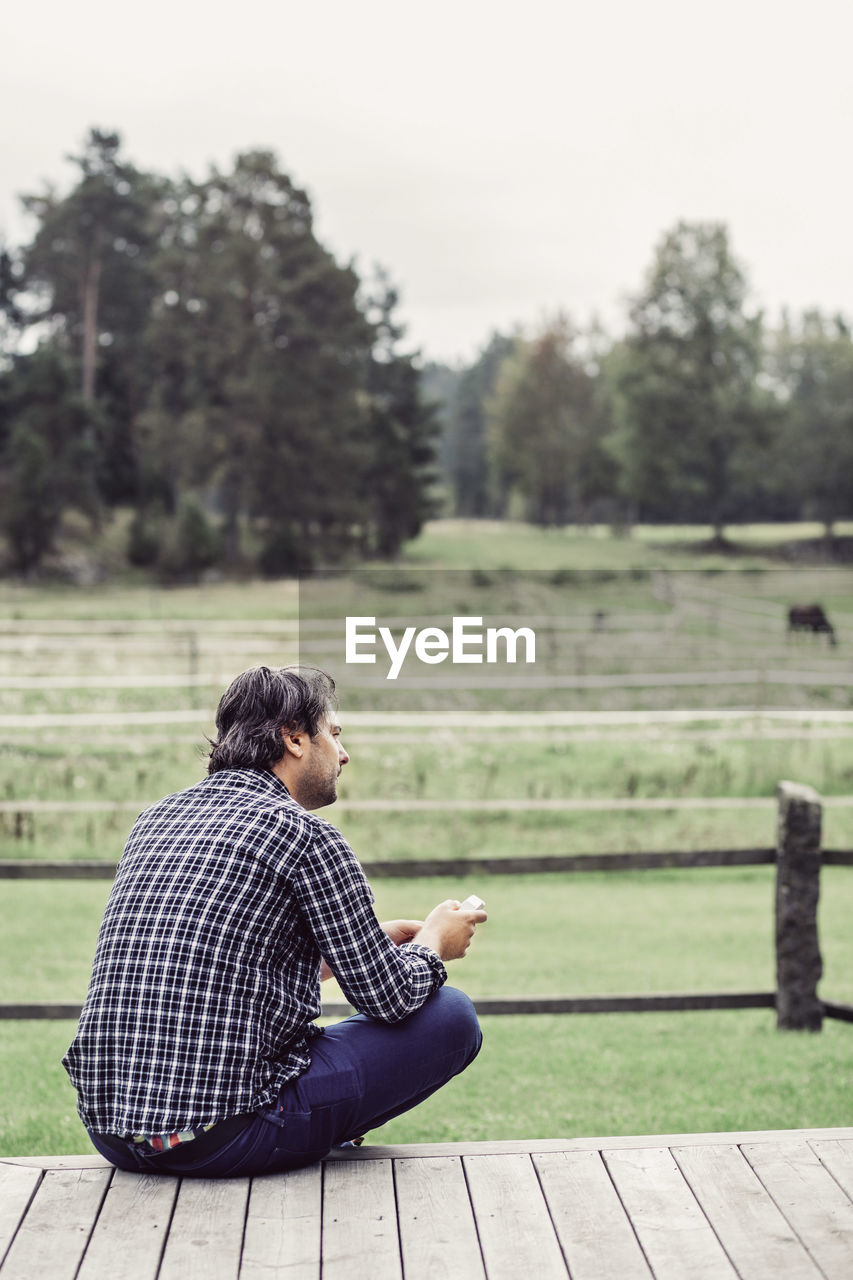 Rear view of male farmer sitting on porch at organic farm