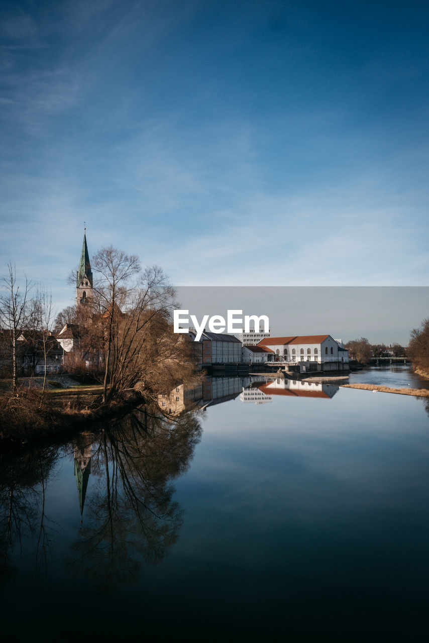 Buildings by river against blue sky