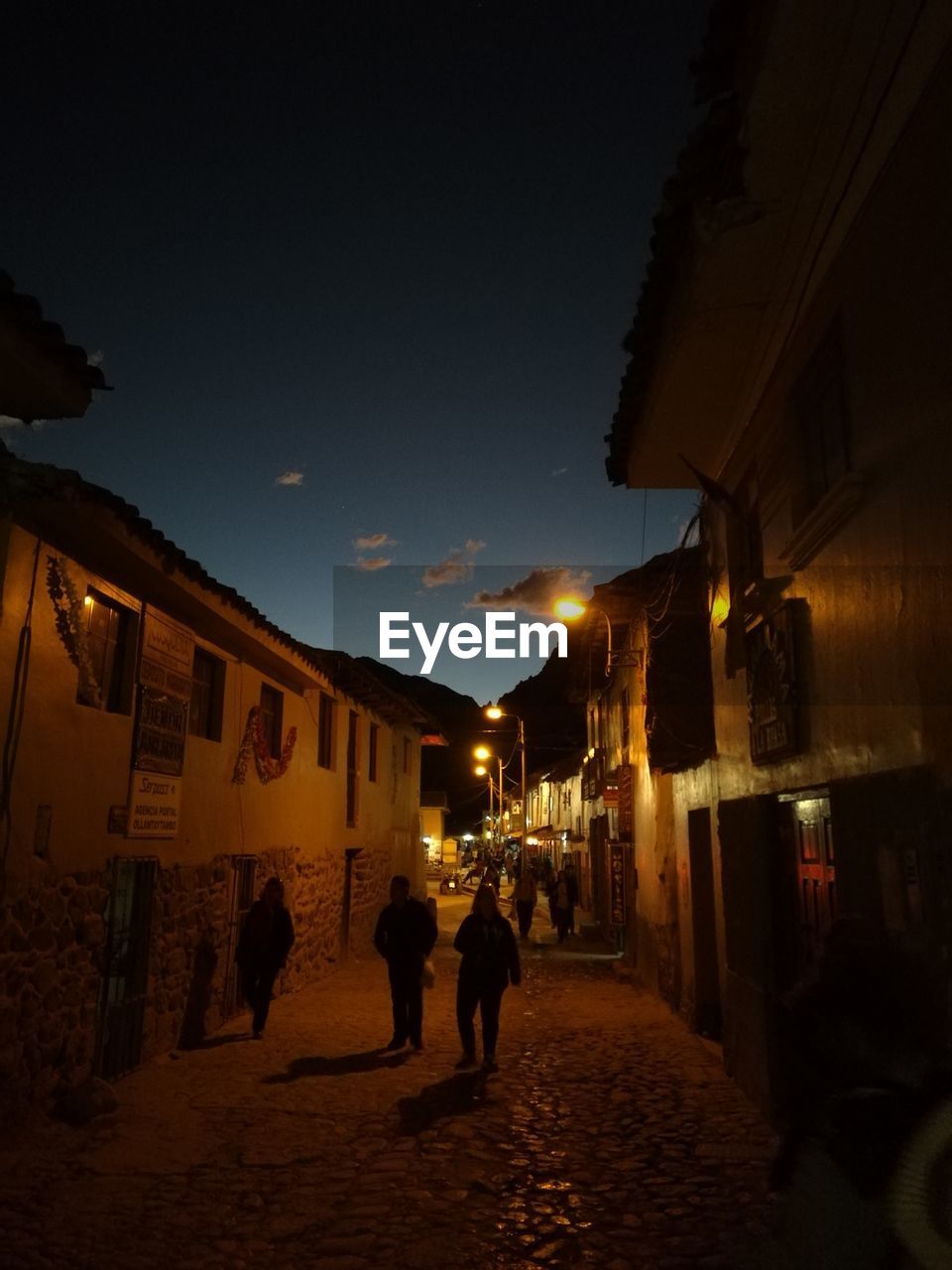 PEOPLE WALKING ON ILLUMINATED STREET AT NIGHT