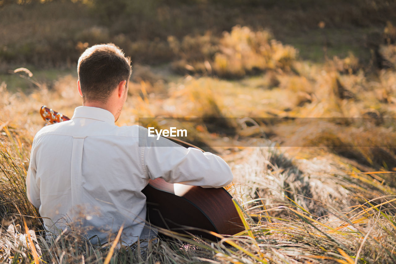Man with acoustic guitar sits in the autumn grass, tranquil scene