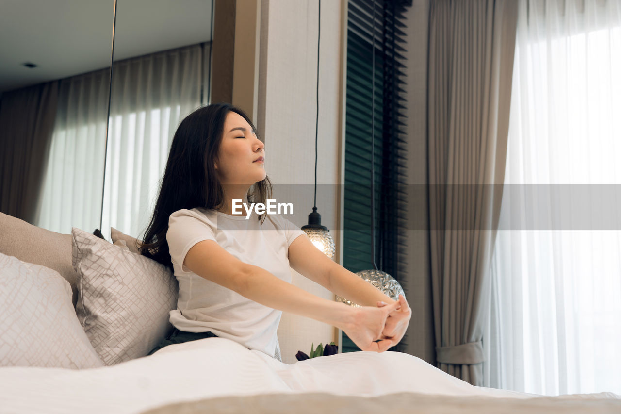 young woman using mobile phone while sitting on bed at home