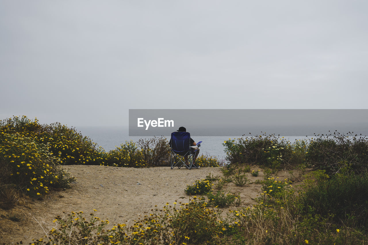 Rear view of man sitting on chair by sea against sky