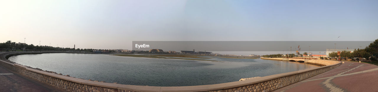 PANORAMIC SHOT OF RIVER BY BUILDINGS AGAINST CLEAR SKY