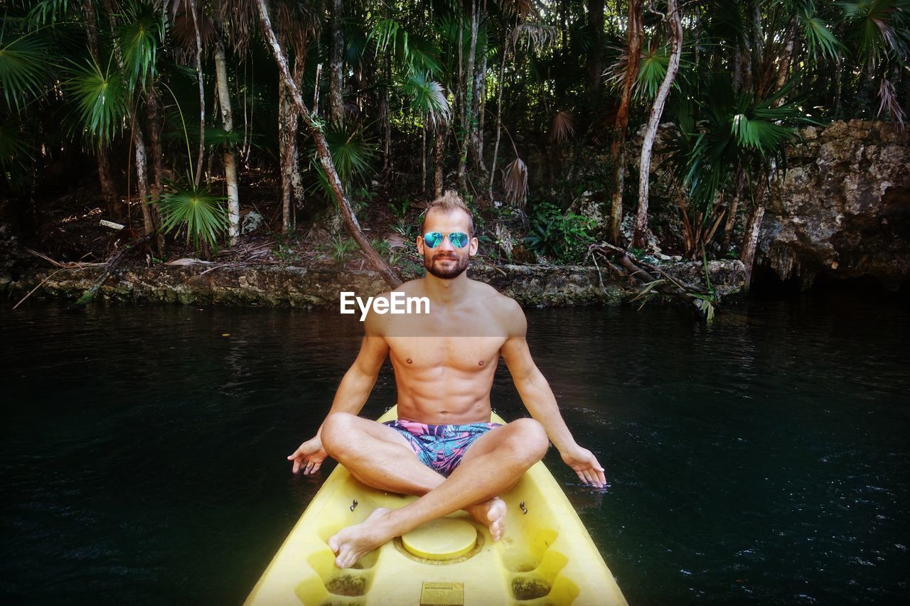 Full length of shirtless man sitting in boat on lake